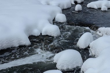 Yoğun karla kaplı büyük kayalar akan bir derede oturur ve yumuşak, yuvarlak şekilli eşsiz bir kış manzarası yaratır..
