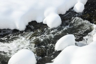 Yoğun karla kaplı büyük kayalar akan bir derede oturur ve yumuşak, yuvarlak şekilli eşsiz bir kış manzarası yaratır..