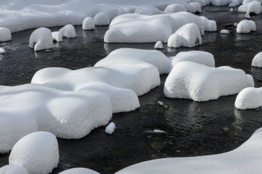 Yoğun karla kaplı büyük kayalar akan bir derede oturur ve yumuşak, yuvarlak şekilli eşsiz bir kış manzarası yaratır..
