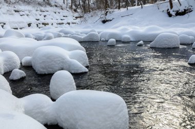 Yoğun karla kaplı büyük kayalar akan bir derede oturur ve yumuşak, yuvarlak şekilli eşsiz bir kış manzarası yaratır..
