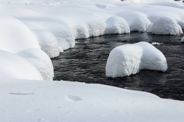 Yoğun karla kaplı büyük kayalar akan bir derede oturur ve yumuşak, yuvarlak şekilli eşsiz bir kış manzarası yaratır..