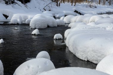 Yoğun karla kaplı büyük kayalar akan bir derede oturur ve yumuşak, yuvarlak şekilli eşsiz bir kış manzarası yaratır..