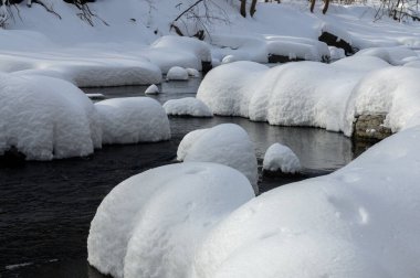 Yoğun karla kaplı büyük kayalar akan bir derede oturur ve yumuşak, yuvarlak şekilli eşsiz bir kış manzarası yaratır..