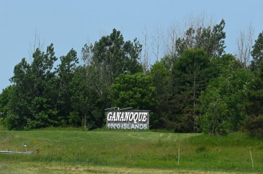 Gananoque, ON, Canada - September 16, 2025: A welcome sign for the town of Gananoque stands on a grassy hill next to a road on a sunny day.