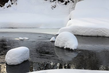 Yoğun karla kaplı büyük kayalar akan bir derede oturur ve yumuşak, yuvarlak şekilli eşsiz bir kış manzarası yaratır..