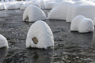 Yoğun karla kaplı büyük kayalar akan bir derede oturur ve yumuşak, yuvarlak şekilli eşsiz bir kış manzarası yaratır..