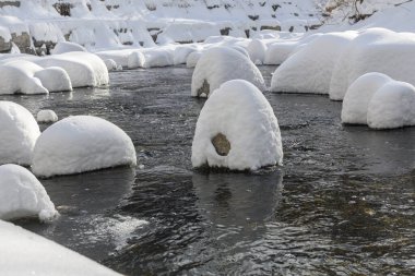 Yoğun karla kaplı büyük kayalar akan bir derede oturur ve yumuşak, yuvarlak şekilli eşsiz bir kış manzarası yaratır..