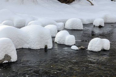 Yoğun karla kaplı büyük kayalar akan bir derede oturur ve yumuşak, yuvarlak şekilli eşsiz bir kış manzarası yaratır..