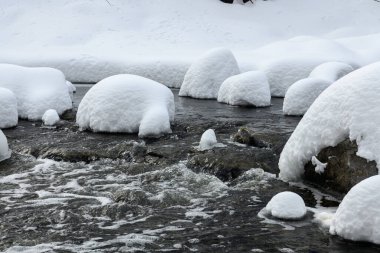 Yoğun karla kaplı büyük kayalar akan bir derede oturur ve yumuşak, yuvarlak şekilli eşsiz bir kış manzarası yaratır..