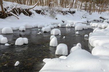 Yoğun karla kaplı büyük kayalar akan bir derede oturur ve yumuşak, yuvarlak şekilli eşsiz bir kış manzarası yaratır..