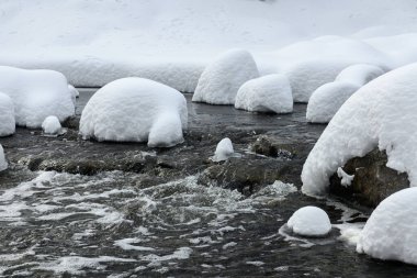 Yoğun karla kaplı büyük kayalar akan bir derede oturur ve yumuşak, yuvarlak şekilli eşsiz bir kış manzarası yaratır..