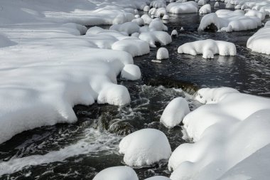 Yoğun karla kaplı büyük kayalar akan bir derede oturur ve yumuşak, yuvarlak şekilli eşsiz bir kış manzarası yaratır..