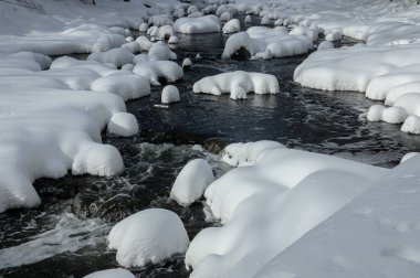 Yoğun karla kaplı büyük kayalar akan bir derede oturur ve yumuşak, yuvarlak şekilli eşsiz bir kış manzarası yaratır..