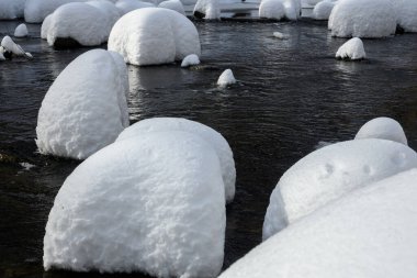 Yoğun karla kaplı büyük kayalar akan bir derede oturur ve yumuşak, yuvarlak şekilli eşsiz bir kış manzarası yaratır..