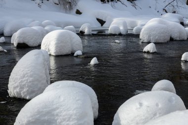Yoğun karla kaplı büyük kayalar akan bir derede oturur ve yumuşak, yuvarlak şekilli eşsiz bir kış manzarası yaratır..