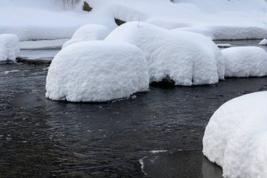Yoğun karla kaplı büyük kayalar akan bir derede oturur ve yumuşak, yuvarlak şekilli eşsiz bir kış manzarası yaratır..