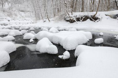 Yoğun karla kaplı büyük kayalar akan bir derede oturur ve yumuşak, yuvarlak şekilli eşsiz bir kış manzarası yaratır..