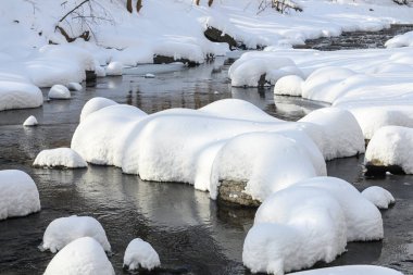 Yoğun karla kaplı büyük kayalar akan bir derede oturur ve yumuşak, yuvarlak şekilli eşsiz bir kış manzarası yaratır..