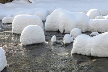 Yoğun karla kaplı büyük kayalar akan bir derede oturur ve yumuşak, yuvarlak şekilli eşsiz bir kış manzarası yaratır..