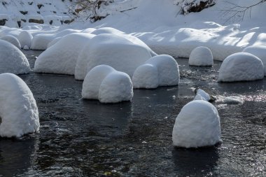 Yoğun karla kaplı büyük kayalar akan bir derede oturur ve yumuşak, yuvarlak şekilli eşsiz bir kış manzarası yaratır..