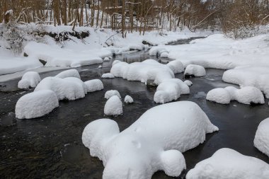 Yoğun karla kaplı büyük kayalar akan bir derede oturur ve yumuşak, yuvarlak şekilli eşsiz bir kış manzarası yaratır..