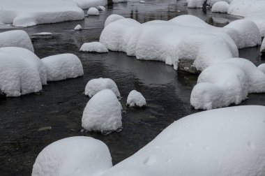 Yoğun karla kaplı büyük kayalar akan bir derede oturur ve yumuşak, yuvarlak şekilli eşsiz bir kış manzarası yaratır..