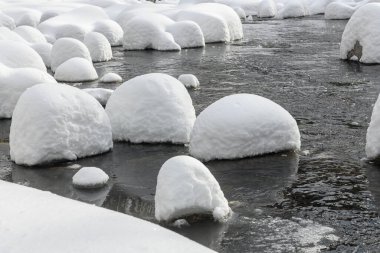 Yoğun karla kaplı büyük kayalar akan bir derede oturur ve yumuşak, yuvarlak şekilli eşsiz bir kış manzarası yaratır..