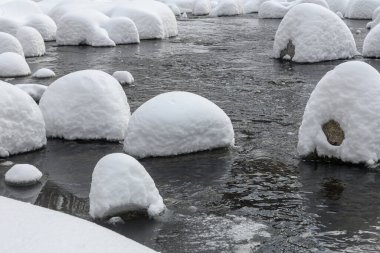 Yoğun karla kaplı büyük kayalar akan bir derede oturur ve yumuşak, yuvarlak şekilli eşsiz bir kış manzarası yaratır..