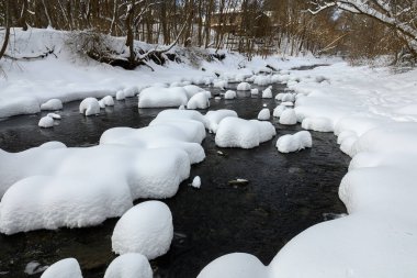 Yoğun karla kaplı büyük kayalar akan bir derede oturur ve yumuşak, yuvarlak şekilli eşsiz bir kış manzarası yaratır..
