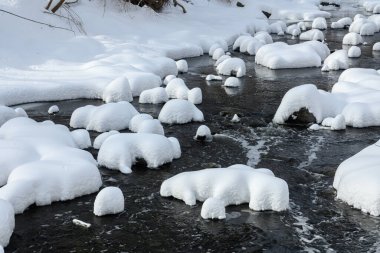 Yoğun karla kaplı büyük kayalar akan bir derede oturur ve yumuşak, yuvarlak şekilli eşsiz bir kış manzarası yaratır..