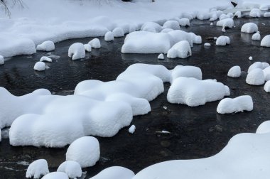 Yoğun karla kaplı büyük kayalar akan bir derede oturur ve yumuşak, yuvarlak şekilli eşsiz bir kış manzarası yaratır..
