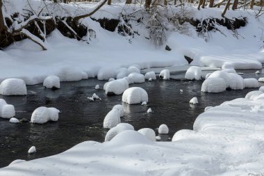 Yoğun karla kaplı büyük kayalar akan bir derede oturur ve yumuşak, yuvarlak şekilli eşsiz bir kış manzarası yaratır..