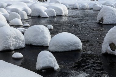 Yoğun karla kaplı büyük kayalar akan bir derede oturur ve yumuşak, yuvarlak şekilli eşsiz bir kış manzarası yaratır..