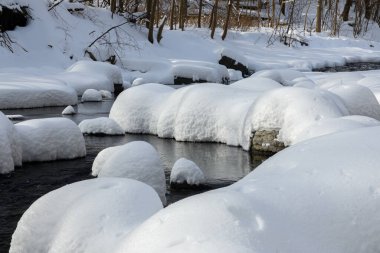 Yoğun karla kaplı büyük kayalar akan bir derede oturur ve yumuşak, yuvarlak şekilli eşsiz bir kış manzarası yaratır..