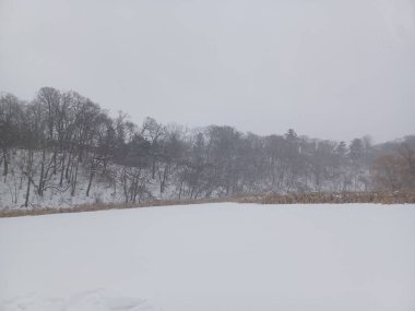 Geniş, açık bir vadi ya da donmuş nehir yatağı, bulutlu bir kış gününde tamamen derin, beyaz kar ve ayak izleriyle kaplıdır..