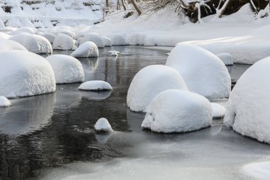 Yoğun karla kaplı büyük kayalar akan bir derede oturur ve yumuşak, yuvarlak şekilli eşsiz bir kış manzarası yaratır..