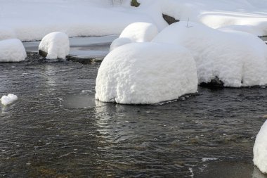 Yoğun karla kaplı büyük kayalar akan bir derede oturur ve yumuşak, yuvarlak şekilli eşsiz bir kış manzarası yaratır..