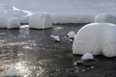 Yoğun karla kaplı büyük kayalar akan bir derede oturur ve yumuşak, yuvarlak şekilli eşsiz bir kış manzarası yaratır..