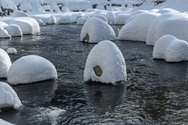 Yoğun karla kaplı büyük kayalar akan bir derede oturur ve yumuşak, yuvarlak şekilli eşsiz bir kış manzarası yaratır..