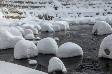 Yoğun karla kaplı büyük kayalar akan bir derede oturur ve yumuşak, yuvarlak şekilli eşsiz bir kış manzarası yaratır..