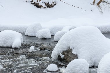 Yoğun karla kaplı büyük kayalar akan bir derede oturur ve yumuşak, yuvarlak şekilli eşsiz bir kış manzarası yaratır..