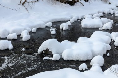 Yoğun karla kaplı büyük kayalar akan bir derede oturur ve yumuşak, yuvarlak şekilli eşsiz bir kış manzarası yaratır..