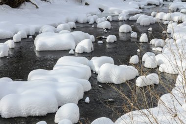 Yoğun karla kaplı büyük kayalar akan bir derede oturur ve yumuşak, yuvarlak şekilli eşsiz bir kış manzarası yaratır..