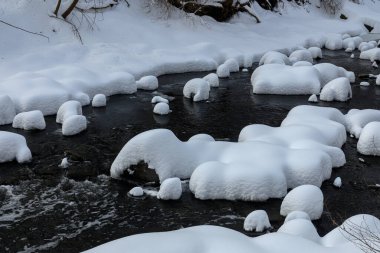 Yoğun karla kaplı büyük kayalar akan bir derede oturur ve yumuşak, yuvarlak şekilli eşsiz bir kış manzarası yaratır..