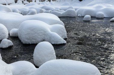 Yoğun karla kaplı büyük kayalar akan bir derede oturur ve yumuşak, yuvarlak şekilli eşsiz bir kış manzarası yaratır..