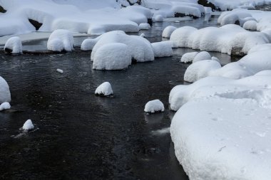 Yoğun karla kaplı büyük kayalar akan bir derede oturur ve yumuşak, yuvarlak şekilli eşsiz bir kış manzarası yaratır..