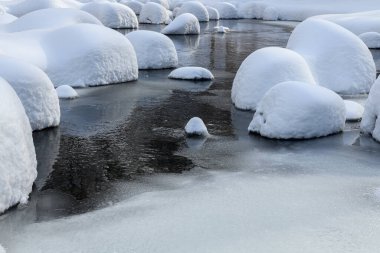 Yoğun karla kaplı büyük kayalar akan bir derede oturur ve yumuşak, yuvarlak şekilli eşsiz bir kış manzarası yaratır..