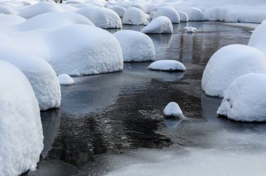 Yoğun karla kaplı büyük kayalar akan bir derede oturur ve yumuşak, yuvarlak şekilli eşsiz bir kış manzarası yaratır..