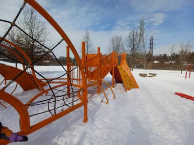 Toronto, ON, Kanada - 6 Aralık 2025: Turuncu metal ve halat tırmanma yapısı parlak bir kış günü karla kaplı bir çocuk parkında boş duruyor.