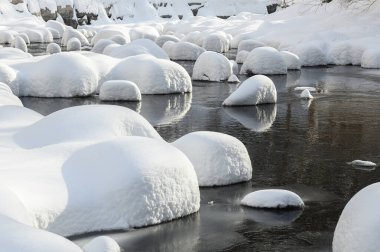 Yoğun karla kaplı büyük kayalar akan bir derede oturur ve yumuşak, yuvarlak şekilli eşsiz bir kış manzarası yaratır..